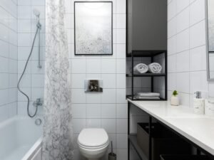 Interior of light bathroom with toilet near bathtub with shower and curtain near counter with shelves with towels and containers and decorative objects near white tile